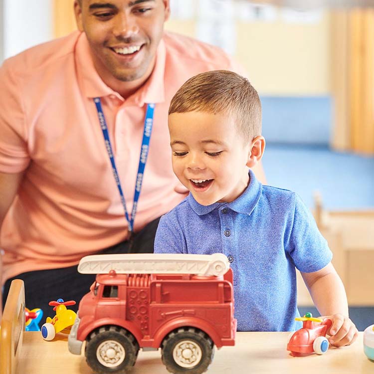 man and preschooler playing with a toy truck in a classroom